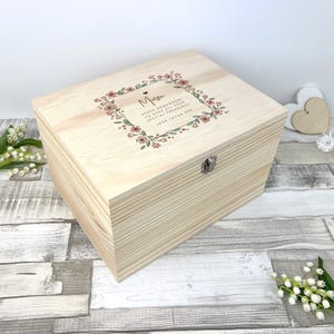 Peut inclure: Un coffret souvenir en bois de couleur claire avec un couvercle à charnière et un fermoir en métal. Le couvercle présente une couronne florale avec le mot "Mum" et d'autres textes. La boîte est rectangulaire et présente un grain de bois visible.