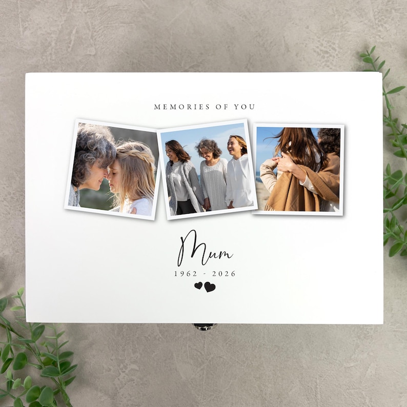 May include: A white wooden box with three framed photos. The photos show a woman with others. The text "MEMORIES OF YOU" is above the photos. The word "Mum" is written in cursive, with the years 1962-2026 below it, along with two heart symbols.