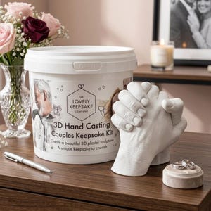 May include: A white 3D hand casting kit with the text "THE LOVELY KEEPSAKE COMPANY" and "3D Hand Casting Couples Keepsake Kit". A white plaster sculpture of clasped hands and a small round ring holder with two rings are also visible.