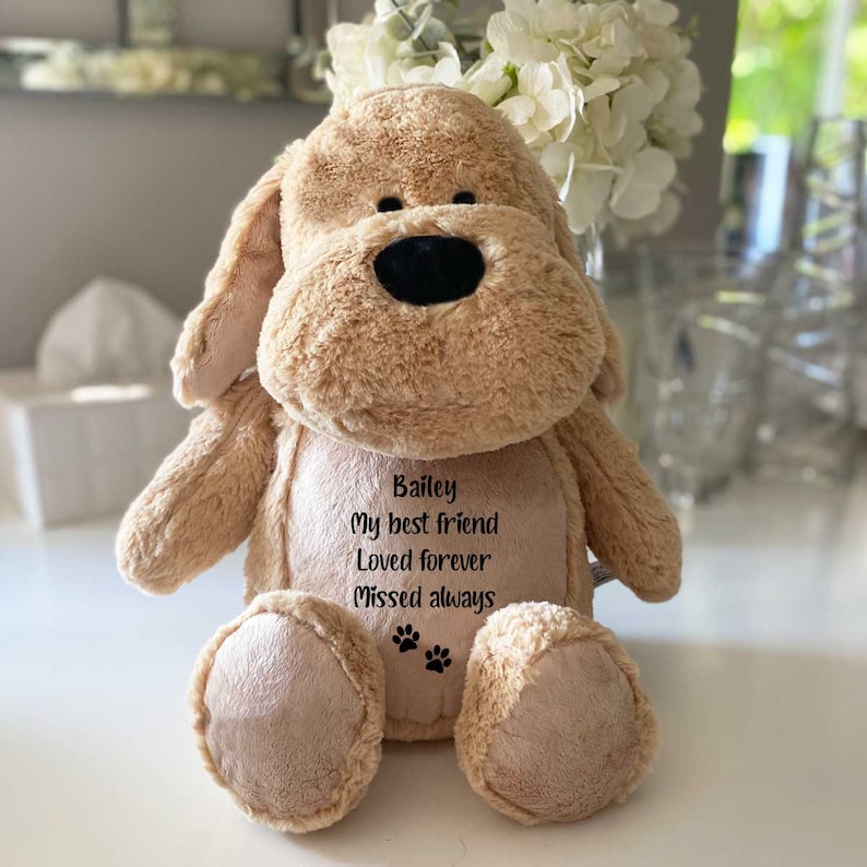 May include: A beige plush dog toy with embroidered text that reads "Bailey My best friend Loved forever Missed always" and paw prints.