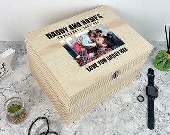May include: A rectangular light-colored wooden keepsake box with a hinged lid featuring a printed photograph of a person holding a child. The text DADDY AND ROSIE'S ADVENTURES TOGETHER and LOVE YOU DADDY XXX is printed in black on the wooden lid surface.