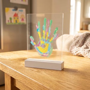 May include: A clear acrylic rectangular plaque featuring a colorful handprint in shades of yellow, pink, blue, and green. The plaque is mounted vertically into a solid white rectangular base, creating a freestanding display piece for home decor.