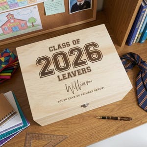 Peut inclure: Une boîte à souvenirs rectangulaire en bois clair avec le texte gravé CLASS OF 2026 LEAVERS, le prénom William et SOUTH CAVE CE PRIMARY SCHOOL. La boîte possède un fermoir métallique sur le devant et une finition en bois naturel lisse.