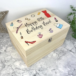 May include: A wooden box with a hinged lid, decorated with illustrations of fashion items and the text "Happy 60th Birthday Nana!". The box has a silver clasp and is adorned with images of a red dress, perfume bottles, and high heels.