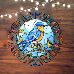 May include: A stained glass wind chime featuring a bluebird with yellow accents perched on a branch with green leaves. The wind chime is circular and has a decorative metal frame.