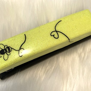 May include: A yellow glitter stapler with a black bee and heart design.