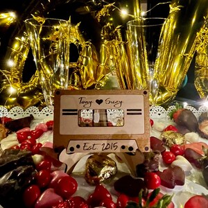 May include: A wooden cassette tape stand with the text "Tony ♥ Suzy Est. 2015" on it. The stand is surrounded by chocolate, candy hearts, and strawberries.
