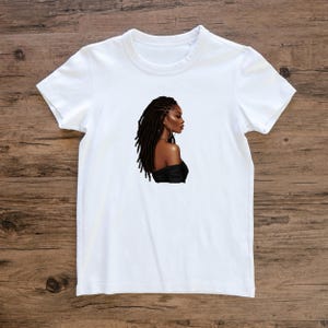 Puede incluir: Camiseta blanca con un gr&aacute;fico de una mujer con largas rastas marrones y un top negro de hombros descubiertos.