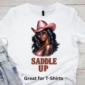May include: A white t-shirt with a graphic of a woman wearing a pink cowboy hat and sunglasses. The text "Saddle Up" is printed in brown letters below the graphic. The text "Great for T-Shirts" is printed at the bottom of the shirt.