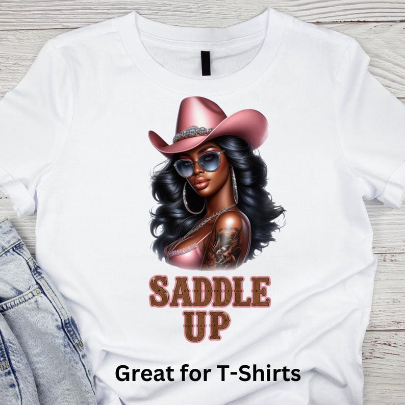 May include: A white t-shirt with a graphic of a woman wearing a pink cowboy hat and sunglasses. The text "Saddle Up" is printed in brown letters below the graphic. The text "Great for T-Shirts" is printed at the bottom of the shirt.