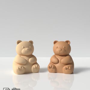 Puede incluir: Dos figuritas de osito de peluche impresas en 3D, una de color marrón claro y la otra de color marrón oscuro. Los ositos están sentados con las patas delante de ellos.