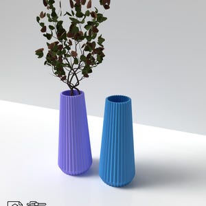 May include: Two ceramic vases, one light blue and one lavender, with a ribbed design. A small leafy branch with brown leaves is in the lavender vase.