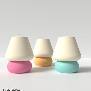 Può includere: Tre candele a forma di fungo dai colori pastello. Ogni candela ha una parte superiore color crema e una base arrotondata in rosa, giallo e blu. Le candele sono disposte su una superficie bianca. L'immagine include anche icone 3D e STL.