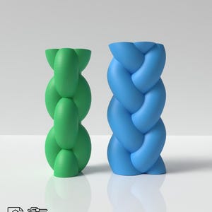 May include: Two 3D printed vases, one green and one blue, with a braided design. The vases are on a white surface.