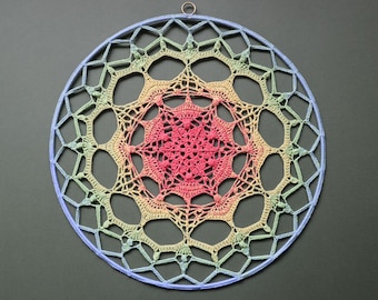 May include: A handmade, circular dream catcher with a gradient of colors. The center is a vibrant pink, transitioning to yellow, green, and blue towards the outer edge. The design features intricate crochet work and a light blue outer ring.