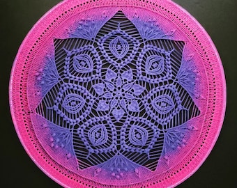 Può includere: Un mandala all'uncinetto viola e rosa con effetto sfumato. Il mandala è circolare e presenta un design delicato e intricato.