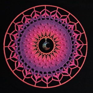 May include: A pink and purple crocheted mandala wall hanging with a crescent moon charm in the center.