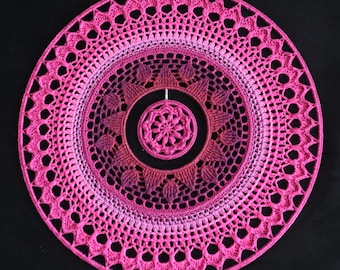 Può includere: Un grande mandala all'uncinetto rosa e bianco con un mandala all'uncinetto rosa più piccolo al centro. Il mandala è realizzato con una varietà di punti e ha un aspetto delicato e traforato.