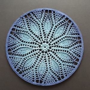 Könnte beinhalten: Eine blaue und weiße gehäkelte Tischdecke mit einem runden Design. Die Tischdecke hat ein zartes, spitzenartiges Muster und ist perfekt, um jedem Tisch eine elegante Note zu verleihen.