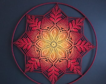 May include: A handmade, crochet wall hanging featuring a vibrant, star-shaped design. The piece showcases a gradient of colors, transitioning from a warm yellow center to shades of orange and red at the edges. The circular frame adds a finished look.