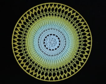 Puede incluir: Un mandala tejido a crochet con un diseño degradado en amarillo y azul. El mandala tiene un diseño floral central y está rodeado de una serie de círculos concéntricos.