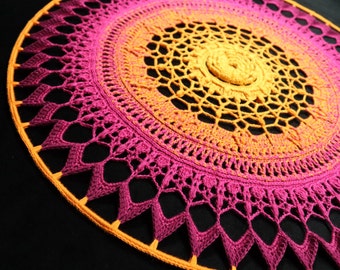 May include: A large, round crochet mandala with a gradient of pink and orange colors. The center of the mandala is a smaller, yellow circle.