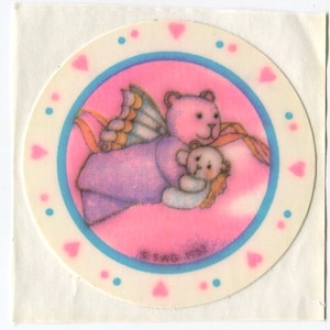 K&ouml;nnte beinhalten: Ein runder rosa und blauer Aufkleber mit einem rosa Teddyb&auml;r mit Schmetterlingsfl&uuml;geln, der einen kleineren Teddyb&auml;r h&auml;lt. Der Aufkleber hat einen wei&szlig;en Rand mit rosa Herzen und blauen Punkten.