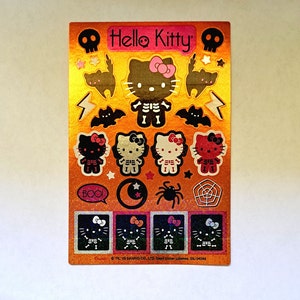 May include: A sheet of colorful Hello Kitty Halloween stickers featuring a skeleton Hello Kitty, bats, spiders, and a moon. The stickers are on a gold background with glitter accents. The text "Hello Kitty" and "BOO!" are included on the sheet.