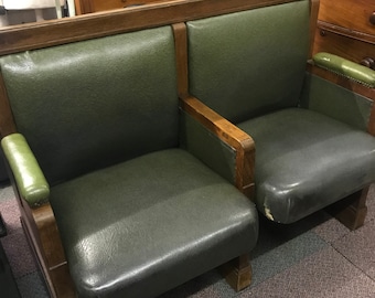 Könnte beinhalten: Eine zweisitzige Vintage-Bank mit olivgrüner Lederpolsterung und Holzarmlehnen und -rahmen. Die Bank hat ein klassisches Design mit hohem Rücken und gepolsterten Sitzen. Der Holzrahmen hat eine dunkle Oberfläche, und das Leder weist Gebrauchsspuren auf.