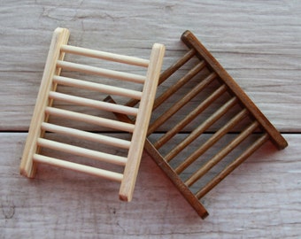 May include: Two wooden soap dishes, one light brown and one dark brown, with a slatted design. The dishes are stacked on top of each other.