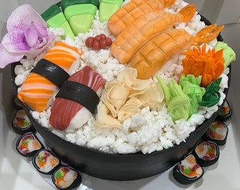 Puede incluir: Un pastel de sushi negro y blanco con una variedad de ingredientes de sushi, incluyendo camarones, aguacate y cangrejo de imitación. El pastel está decorado con una orquídea rosa y hojas verdes. El pastel está rodeado de rollos de sushi individuales.