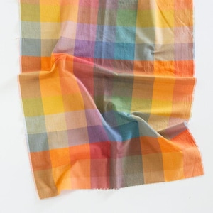 Puede incluir: Una colorida tela a cuadros en tonos de amarillo, naranja, rojo, morado, verde y azul. La tela está doblada y drapeada, mostrando los diversos colores y la textura del material. La tela tiene un aspecto suave y ligeramente arrugado.