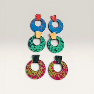 May include: A set of six colorful hoop earrings. Each earring features a circular design with a patterned fabric in blue, green, and pink. The earrings have a rectangular top in red, yellow, and black.