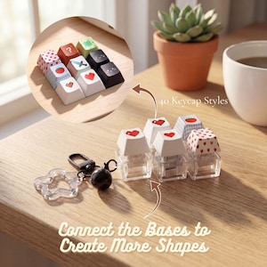 Könnte beinhalten: Eine Sammlung von mechanischen Tastaturkappen mit verschiedenen Designs, darunter pixelige Herzen, eine Tomate, ein Schwert und Muster. Die Tastenkappen haben transparente Kunststoffbasen, die verbunden werden können. Text: 40 Keycap Styles.