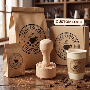 May include: A wooden rubber stamp sits among coffee packaging including a large brown paper bag, a small brown paper bag, a cardboard box, and a white paper cup with a brown sleeve. All items feature a circular Luca's Coffee logo with a cup and beans.