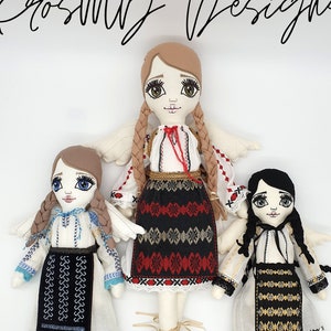 May include: Three handmade fabric dolls wearing traditional Romanian folk costumes. The dolls have long brown hair, black hair, and blonde hair. The dolls are wearing white dresses with embroidered details and colorful skirts. The dolls are standing on a white background.