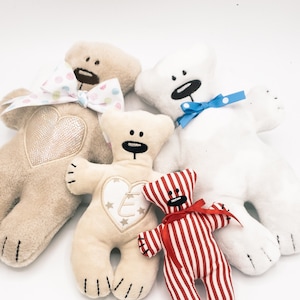 Puede incluir: Cuatro osos de peluche de diferentes colores y patrones. Los osos están todos sentados sobre una superficie blanca. Los osos llevan lazos y tienen corazones bordados en el pecho. Los osos son de diferentes tamaños. El oso más grande es marrón y tiene un lazo de lunares rosa y blanco. El segundo oso más grande es blanco y tiene un lazo azul. El tercer oso más grande es beige y tiene un lazo blanco. El oso más pequeño es rojo y blanco a rayas y tiene un lazo rojo.