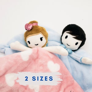 May include: A pink and blue plush blanket with a girl and boy doll. The blanket has white hearts and the text "2 SIZES" and "KrossMB Designs".