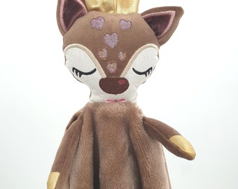 May include: A brown plush deer with gold antlers and pink hearts embroidered on its face. The deer is attached to a brown plush blanket.
