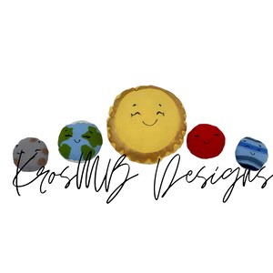 May include: A set of five plush planets, including the sun, earth, mars, and two other planets. The planets have smiling faces and are made of soft, colorful fabric. The sun is yellow, earth is blue and green, mars is red, and the other two planets are gray and blue. The planets are arranged in a line, with the sun in the middle. The text "KrosMB Designs" is visible below the planets.