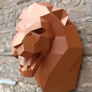 Puede incluir: Una escultura de cabeza de león de papel de color cobre con una expresión feroz. La escultura está hecha de papel doblado y tiene una superficie texturizada.