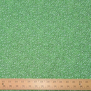May include: Green fabric with a pattern of small white dots. The fabric is a solid green color, and the white dots are scattered across the surface. A wooden ruler is at the bottom of the image, with inch measurements.