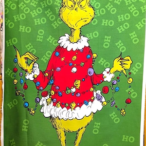 May include: A fabric panel featuring a cartoon Grinch character in a red sweater decorated with colorful lights. The Grinch is holding strands of lights. The background is green with "HO" text. The bottom has "GRINCH" text.