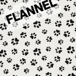 May include: White flannel fabric with a repeating pattern of black paw prints. A white rectangle with the word "FLANNEL" in bold black letters is overlaid on the fabric.
