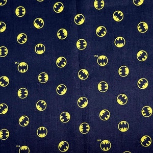 Puede incluir: Tela negra con un patr&oacute;n repetido de logotipos de Batman amarillos. La tela se mide con una regla en pulgadas.