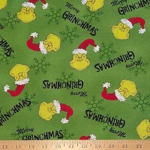 May include: Green fabric with a repeating pattern of a yellow character wearing a red Santa hat and the text "Merry GRINCHMAS". The design also includes snowflakes, creating a festive holiday theme.
