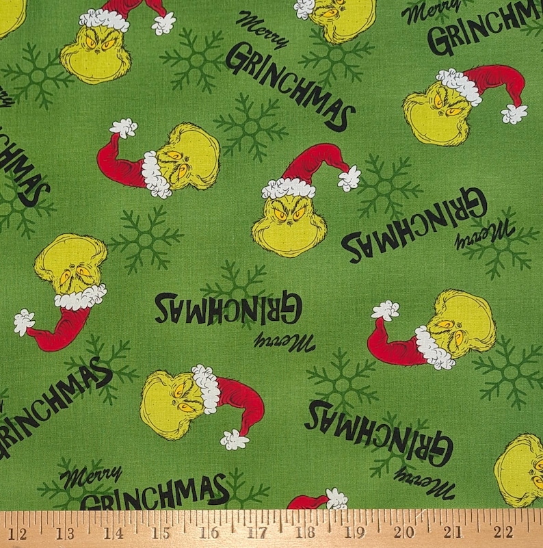May include: Green fabric with a repeating pattern of a yellow character wearing a red Santa hat and the text "Merry GRINCHMAS". The design also includes snowflakes, creating a festive holiday theme.