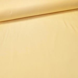 May include: A roll of soft, pale yellow fabric. The material is smooth and appears to be a solid color, with a slight sheen. The fabric is tightly rolled, showing the texture and thickness of the material.