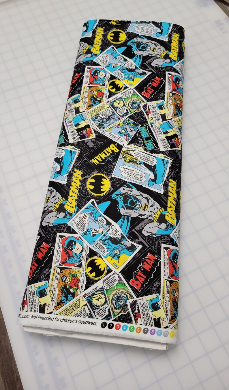 Puede incluir: Tela negra con un patr&oacute;n repetido de vi&ntilde;etas de c&oacute;mics con Batman. Las vi&ntilde;etas son de varios colores, incluyendo rojo, amarillo, azul y verde. El texto "BATMAN" aparece varias veces en la tela.