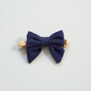 Può includere: Un cerchietto in velluto a coste blu navy con fiocco. Il cerchietto è realizzato in un materiale morbido ed elastico, perfetto per aggiungere un tocco di stile a qualsiasi outfit.